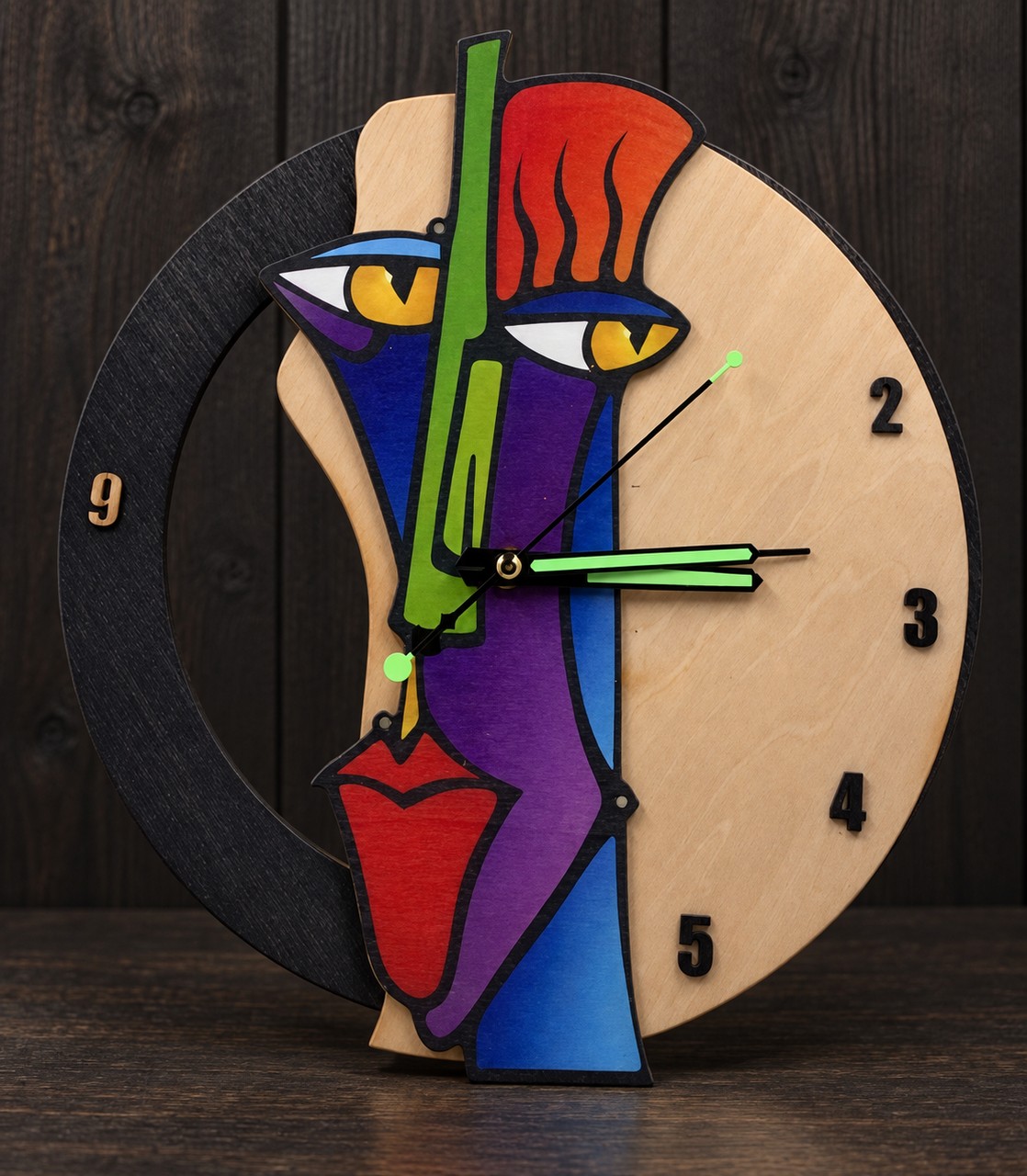 Référence HO 4 — horloge en bois en forme de visage abstrait coloré sur fond studio sombre, diamètre 29 cm